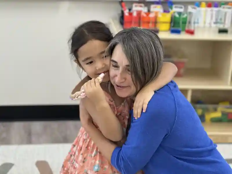 A teacher sharing a warm hug with a child in the classroom